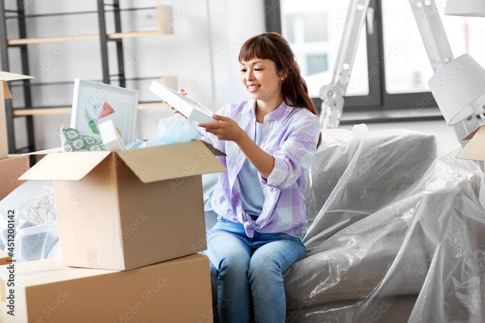 moving, people and real estate concept - happy smiling asian woman unpacking boxes at new home moving, people and real estate concept - happy smiling asian woman unpacking boxes at new home