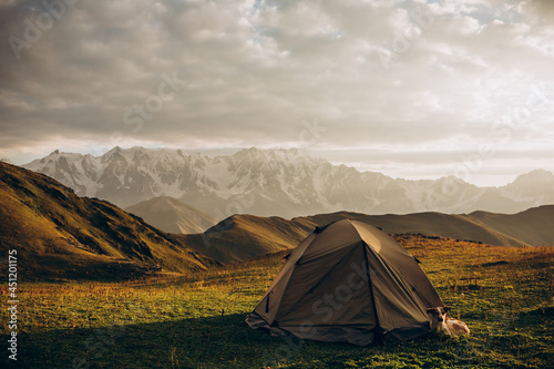 Tourist tent on a hill above the mountains. Dramatic sunset. Summer landscape. The concept of privacy, travel and freedom.