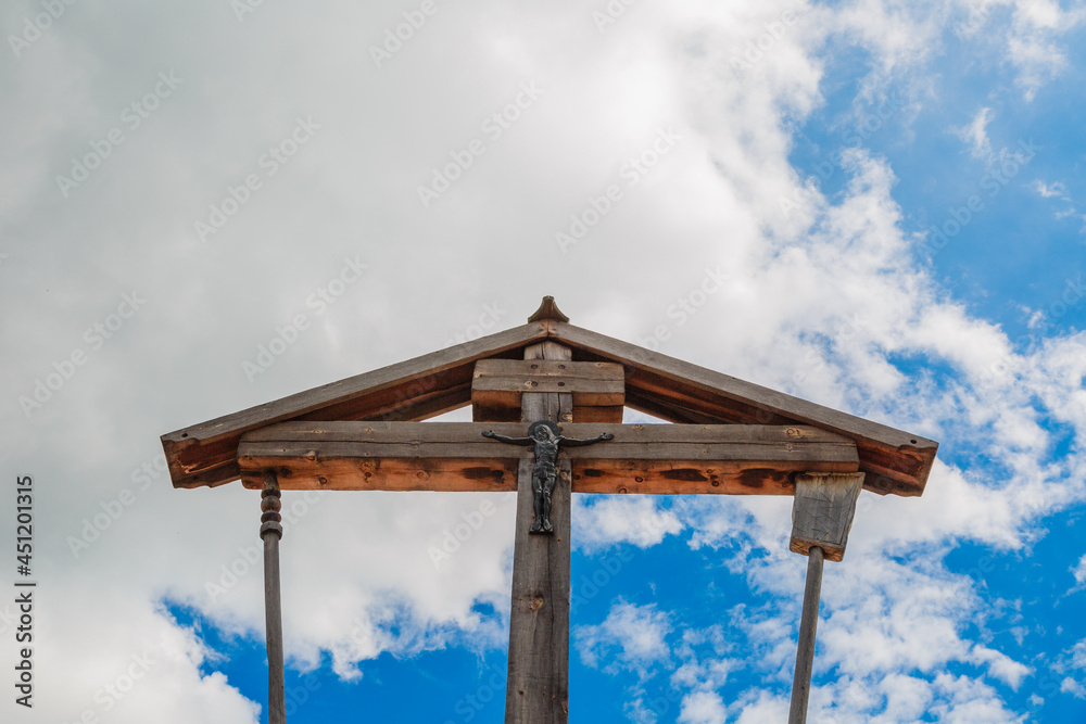 Wooden crucifixion of Jesus Christ on a background of blue sky with clouds.