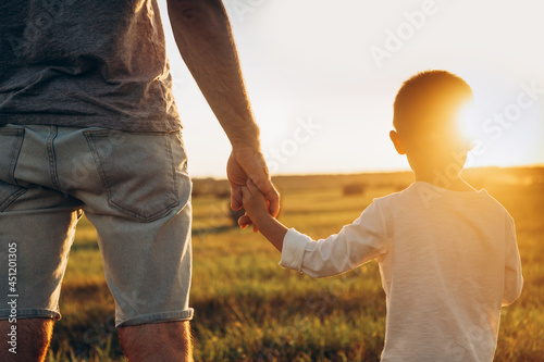 фотографія Father's and his son holding hands at sunset field
