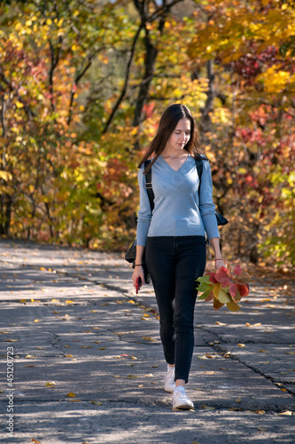 Beautiful young woman is walking along the alley of the autumn park. Young girl in the forest. Vertical frame