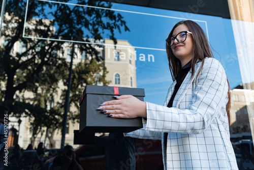 Brunette girl is holding black gift box. Happy young woman with gift in hands. Bottom view. photo