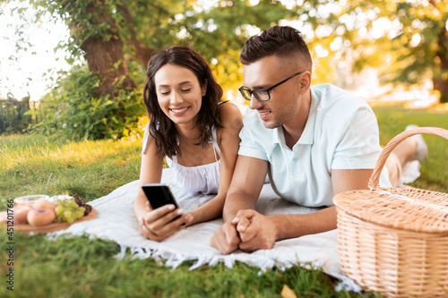 leisure and people concept - happy couple with smartphone having picnic at summer park