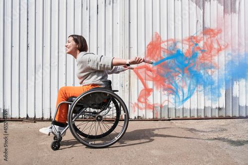 Fototapeta Woman with lower body disability riding at the wheelchair while holding bombs wi