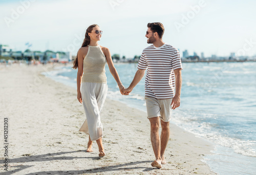 summer holidays and people concept - happy couple walking along beach in tallinn, estonia
