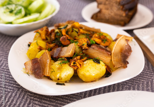 baked potatoes with chanterelles and bacon served with herbs and lightly salted cucumbers on table
