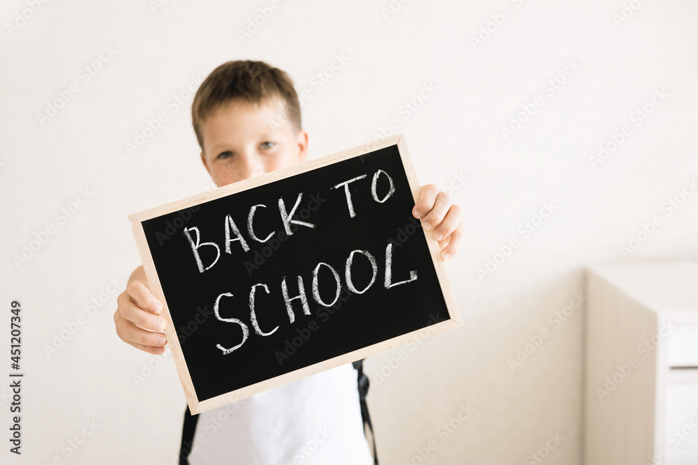 Boy with backpack holding in his hands chalk board with inscription Back to school isolated on white background Boy with backpack holding in his hands chalk board with inscription Back to school isolated on white background