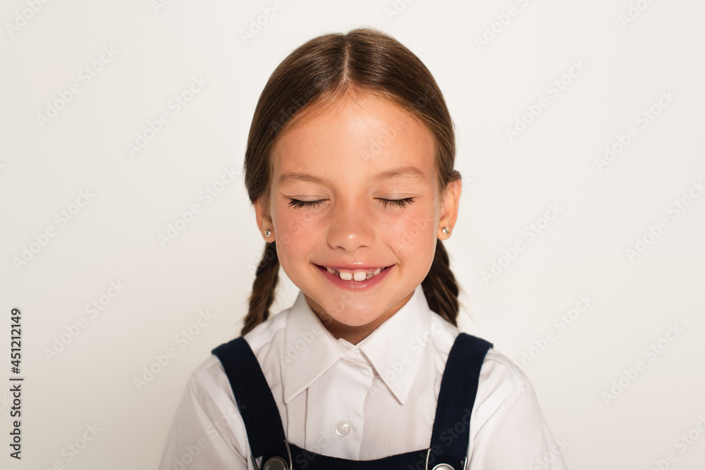 pleased schoolchild smiling with closed eyes isolated on grey pleased schoolchild smiling with closed eyes isolated on grey