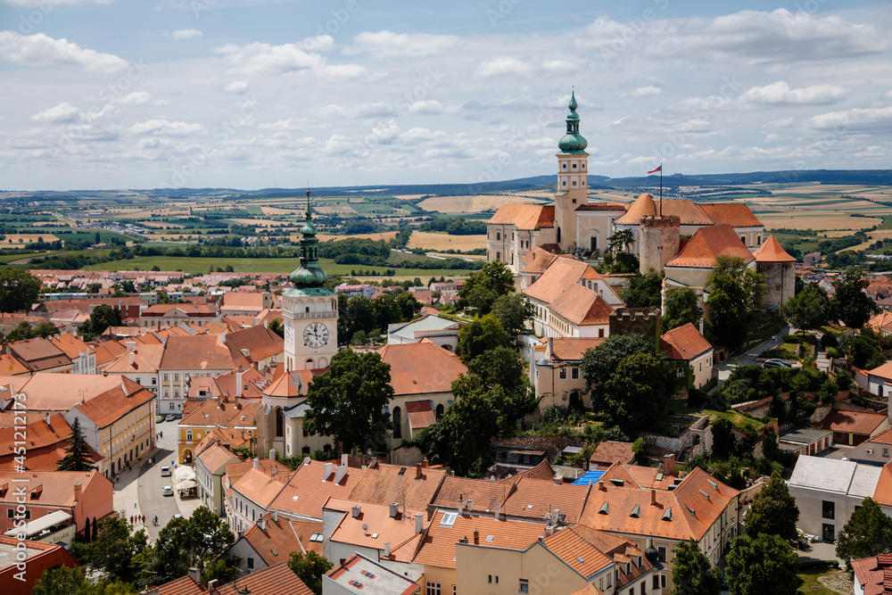 Mikulov, South Moravian Region, Czech Republic, 05 July 2021: Aerial view of medieval town, baroque castle with stone walls on hill, tower of St. Wenceslas church, red tile roofs at sunny summer day