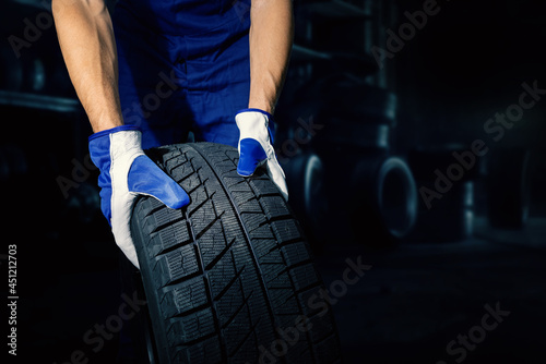 mechanic holding car tire on dark workshop background with copy space. tyre service