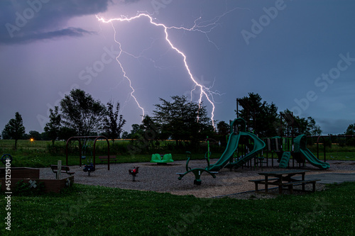 electrical lighting streaks across the sky during thunderstorm moving over children's playground