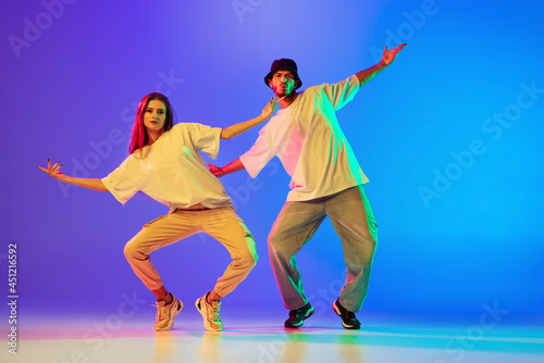 Two young people, guy and girl in casual clothes dancing contemporary dance, hip-hop over blue background in neon light.