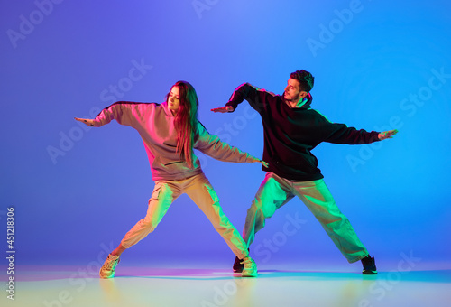 Two young people, man and woman dancing brakedance, hip-hop over blue background in neon light.