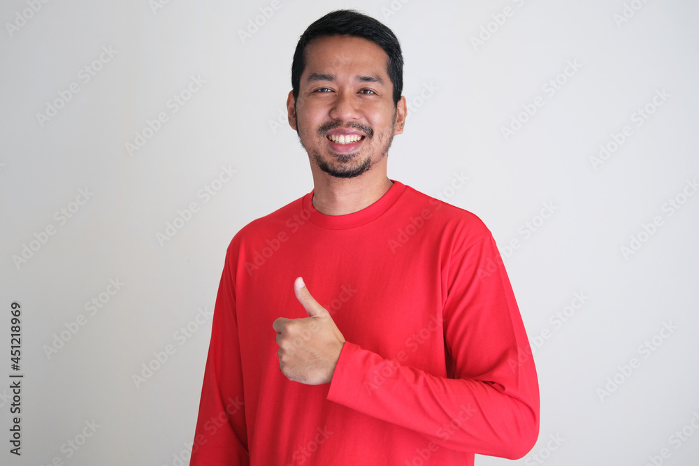 Adult Asian man wearing red clothes smiling happy and giving thumb up Adult Asian man wearing red clothes smiling happy and giving thumb up