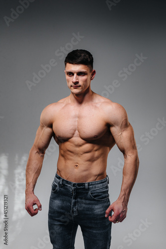 A young sexy athlete with perfect abs poses in the studio topless in jeans on the background. Healthy lifestyle, proper nutrition, training programs and nutrition for weight loss.