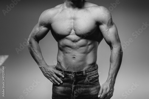 A young sexy athlete with perfect abs poses in the studio topless in jeans. Healthy lifestyle  proper nutrition  training programs and nutrition for weight loss. Black and white.