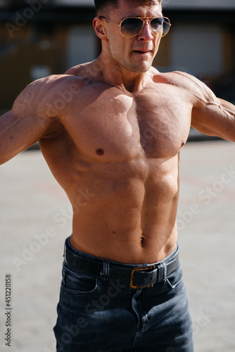 A young sexy athlete with perfect abs trains topless in jeans outside on a sunny day. Healthy lifestyle, proper nutrition, training programs and nutrition for weight loss. © Andrii