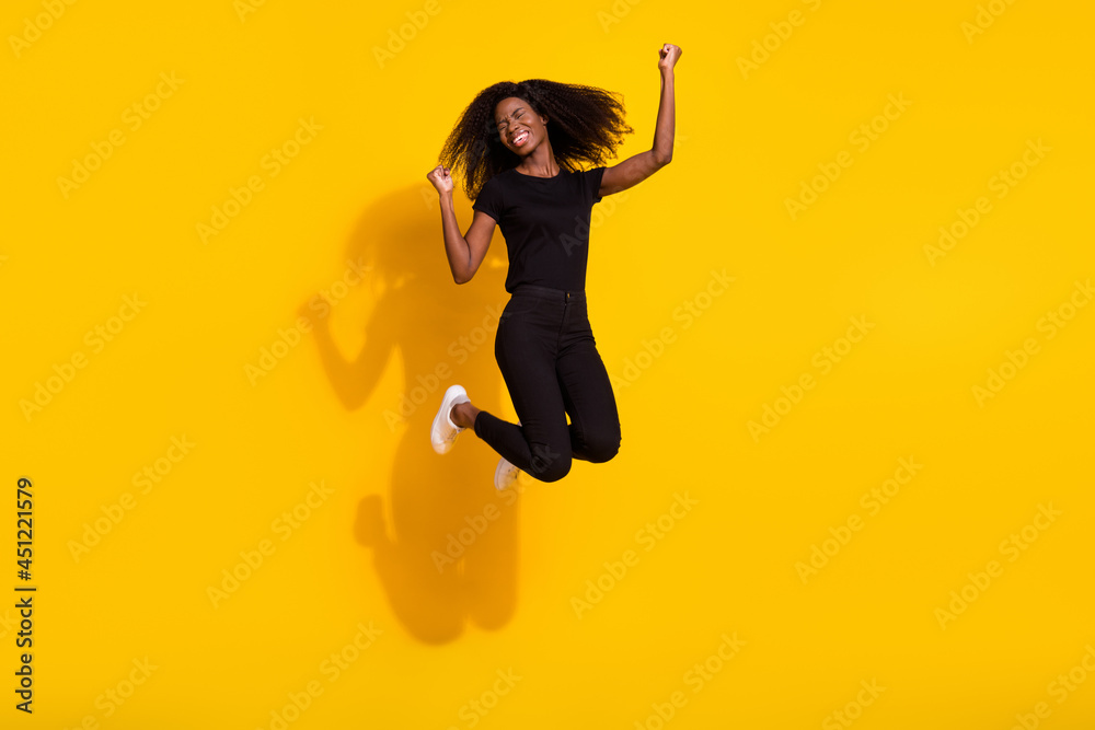 Full size photo of young dark skin happy woman jump up good mood winner isolated on shine yellow color background Full size photo of young dark skin happy woman jump up good mood winner isolated on shine yellow color background