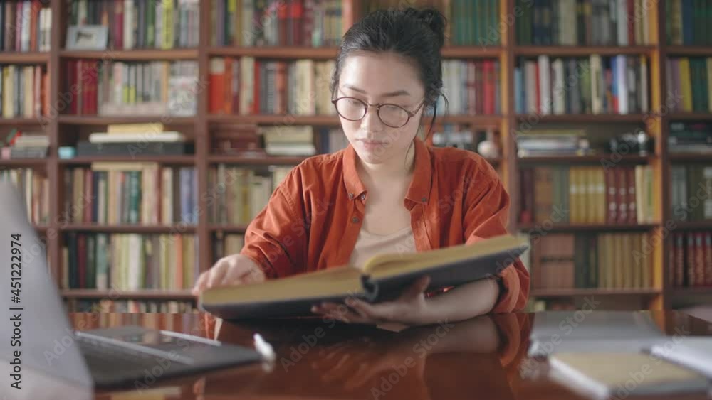 Young asian woman flipping through pages of large book, passionate about reading