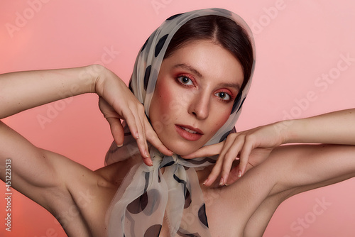 Portrait of a young woman in a fashionable headscarf. Clear skin model with pink makeup. Beauty, fashion, skin care and Spa concept on pink background. photo