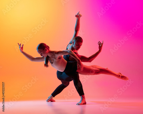 Two dancers, stylish sportive couple, male and female models dancing contemporary dance on colorful gradient yellow pink background in neon light.