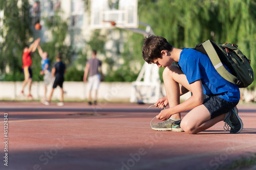 a guy ties his shoelaces on the edge of the field, next to the team playing basketball © soleg
