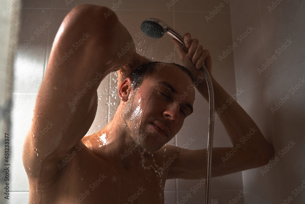 Portrait of young handsome man washes himself with shower gel, lathers head with shampoo in the bathroom at home close-up