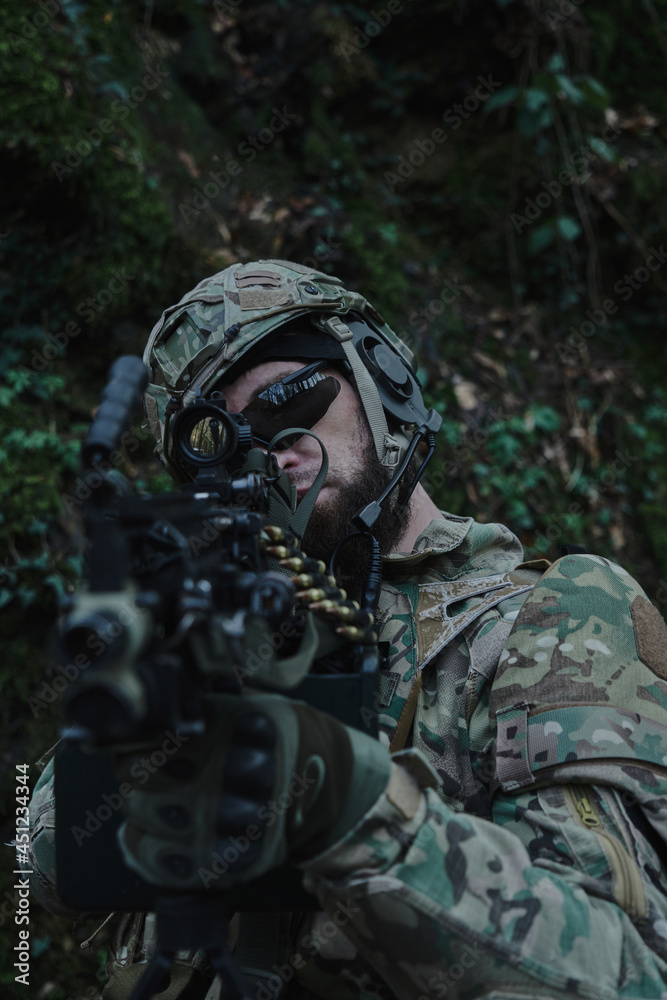 Portrait of airsoft player in professional equipment in helmet aiming at victim with gun in the forest. Soldier with weapons at war