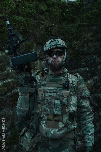 Portrait of airsoft player in professional equipment with machine gun in the forest. Soldier with weapons at war