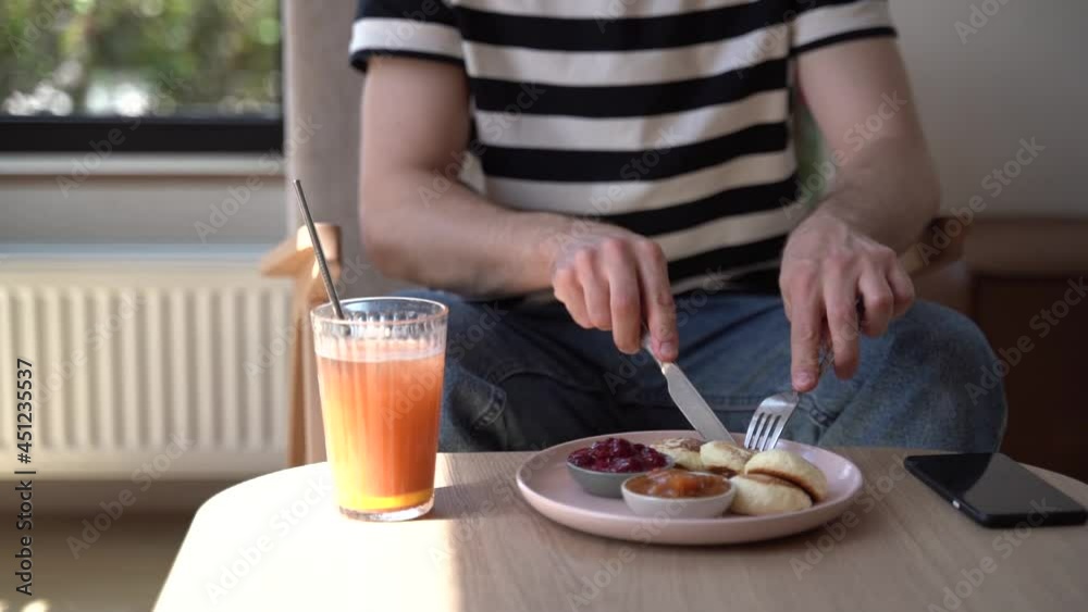 Breakfast, close up view. A man sitting at a small table eating a delicious breakfast. Freshly squeezed juice, jam and cheesecakes Breakfast, close up view. A man sitting at a small table eating a delicious breakfast. Freshly squeezed juice, jam and cheesecakes
