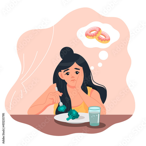 A sad young woman sits at the table with a plate of broccoli and dreams of a donut. Healthy lifestyle and bad habits