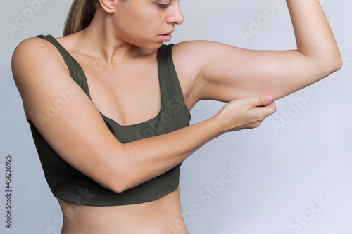 A young caucasian blonde woman grabbing skin on her upper arm with excess fat isolated on a white background. Pinching the loose and saggy muscles. Overweight concept