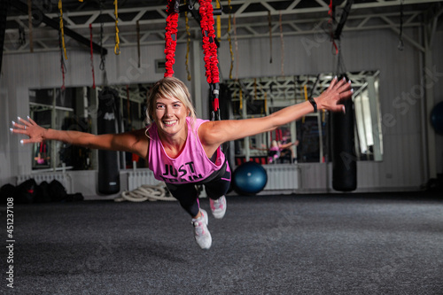 Bungee fitness. Training on loops. A beautiful sports woman in a pink tracksuit trains in the gym with the help of special loops. Poses in limbo