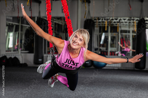 Bungee fitness. Training on loops. A beautiful sports woman in a pink tracksuit trains in the gym with the help of special loops. Poses in limbo