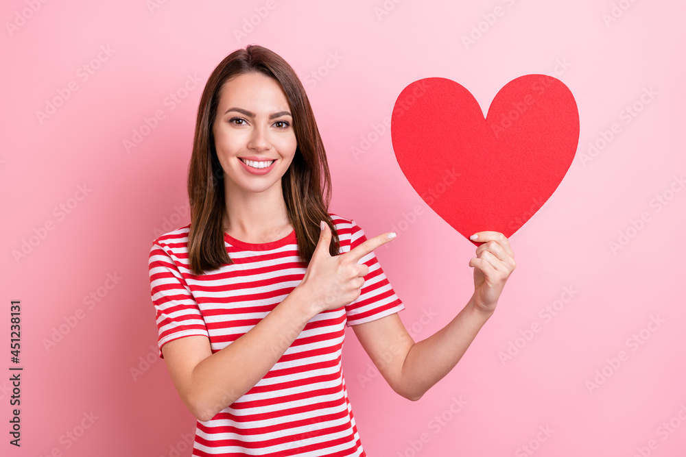 Photo of young cheerful girl happy positive smile point finger paper card heart recommend ad isolated over pink color background Photo of young cheerful girl happy positive smile point finger paper card heart recommend ad isolated over pink color background