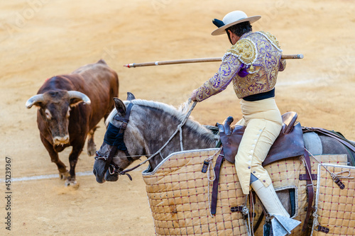 Bullfighter on horse performing on arena with bull photo