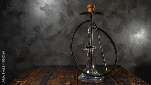 Modern hookah with glass bowl on wooden table. Gray wall background. Lounge concept.