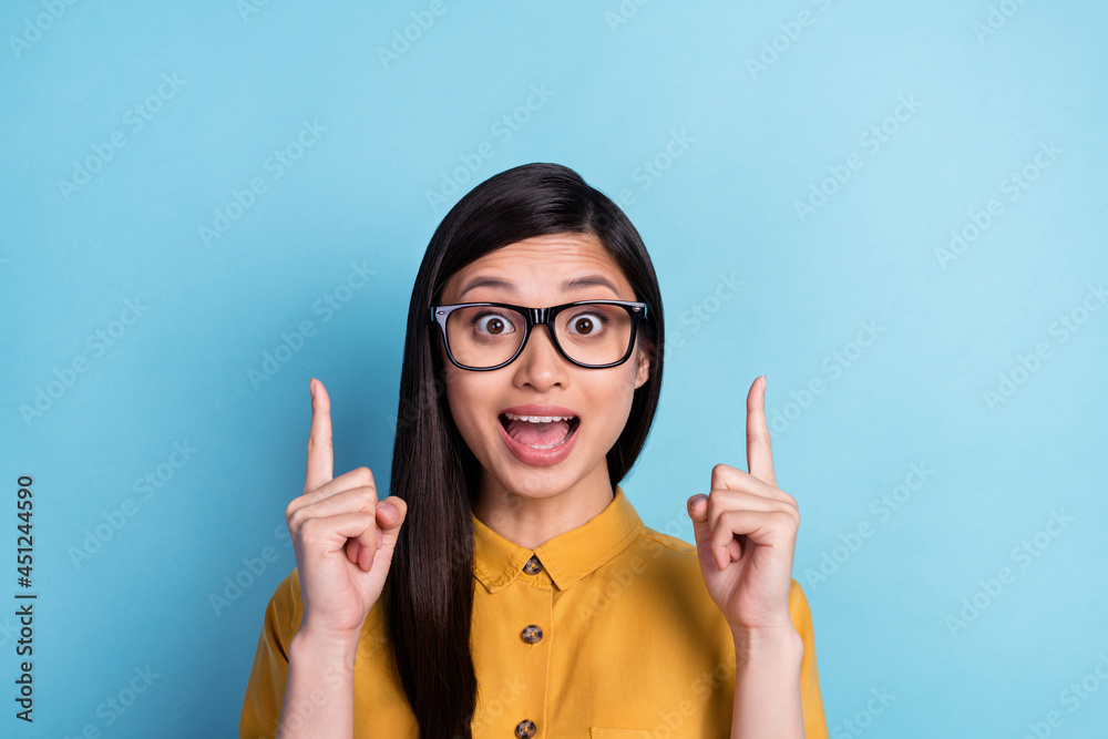 Photo of impressed millennial brunette lady point empty space wear spectacles yellow shirt isolated on blue color background Photo of impressed millennial brunette lady point empty space wear spectacles yellow shirt isolated on blue color background