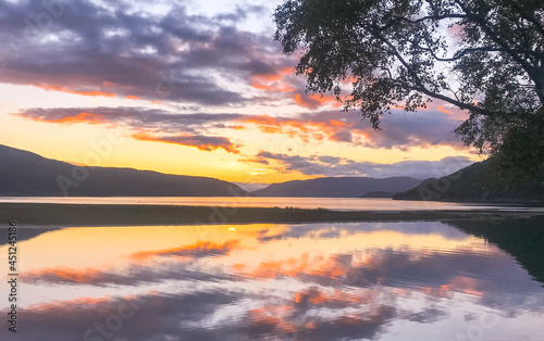 sun setting over the mountains with the reflection in the fjord, midnattsol.