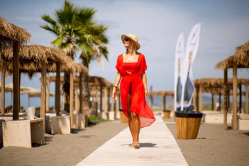 Young woman in red dress walking on a beach at summer