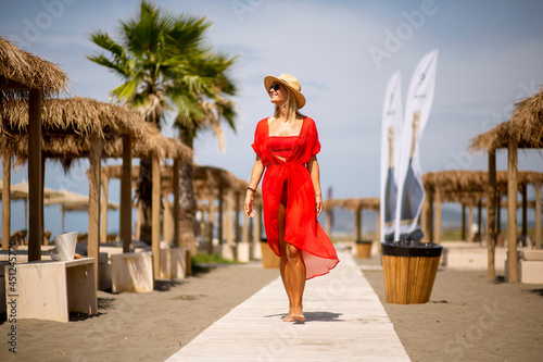 Young woman in red dress walking on a beach at summer