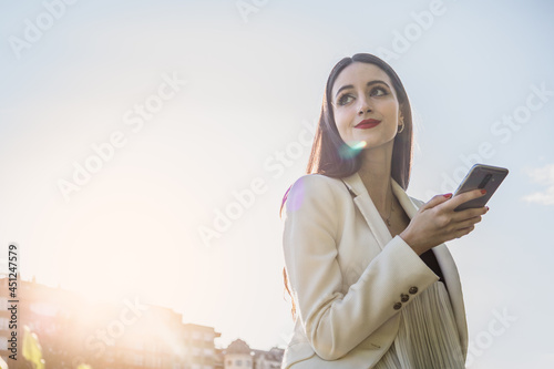 White young woman in formalwear using smartphone. Sunbeam of the sunset. Technology concept photo
