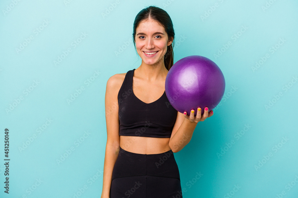 Young caucasian fitness woman holding a ball isolated on blue background happy, smiling and cheerful. Young caucasian fitness woman holding a ball isolated on blue background happy, smiling and cheerful.