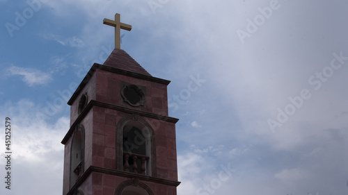 Torre de iglesia católica en cantera rosa con cruz en lo alto photo