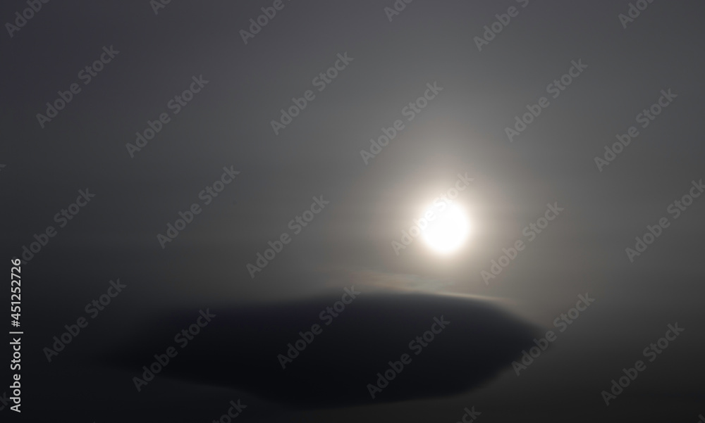 Low-hanging, smooth cloud passing in front of hazy sun creating a mysterious scene