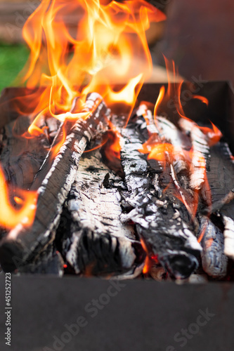 Metal brazier with burning wood and coals in nature on a bright summer sunny day. Bonfire with red flames. Selective focus. Close-up
