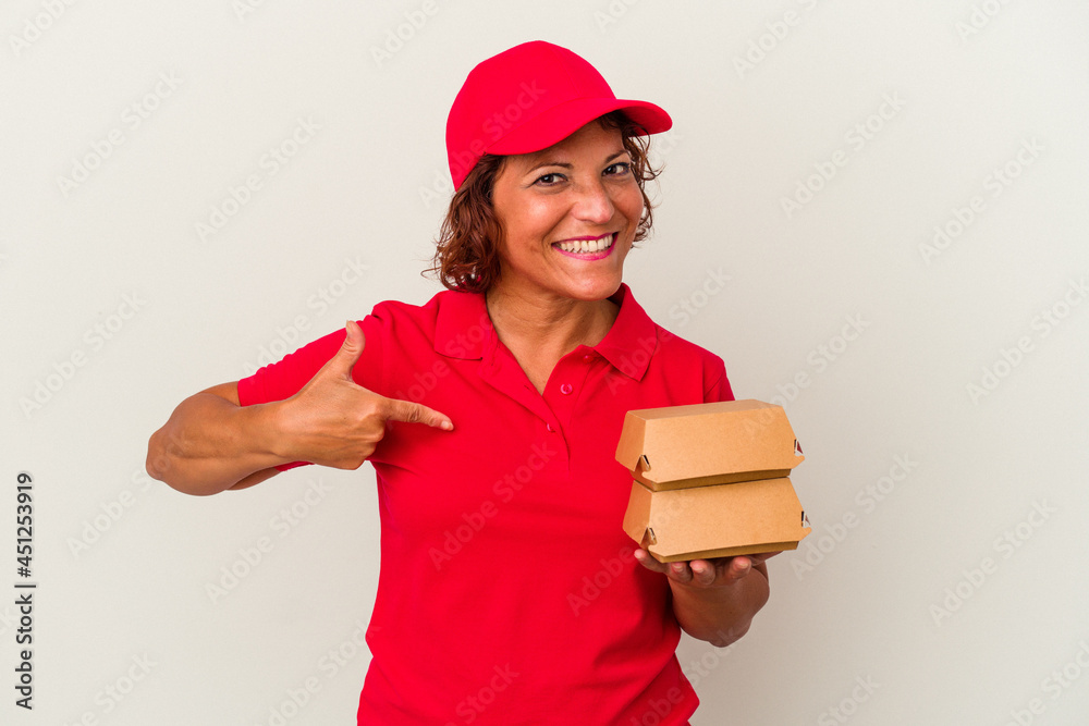 Middle age delivery woman taking burguers isolated on white background person pointing by hand to a shirt copy space, proud and confident Middle age delivery woman taking burguers isolated on white background person pointing by hand to a shirt copy space, proud and confident