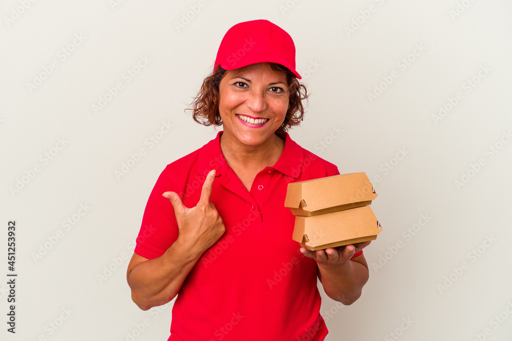Middle age delivery woman taking burguers isolated on white background pointing with finger at you as if inviting come closer. Middle age delivery woman taking burguers isolated on white background pointing with finger at you as if inviting come closer.