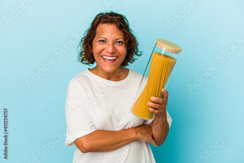 Middle age latin woman holding pasta jar isolated on blue background laughing and having fun.