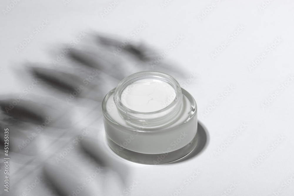 Cosmetic cream or mask in a glass jar with hard shadows from the leaves on a white background. Natural organic care for face and body skin. View from above. Cosmetic cream or mask in a glass jar with hard shadows from the leaves on a white background. Natural organic care for face and body skin. View from above.